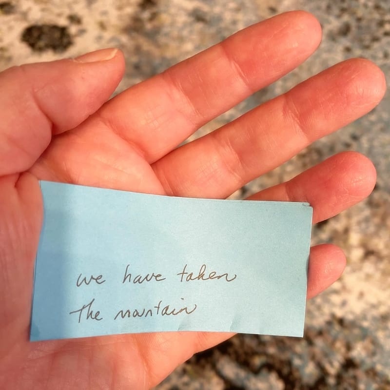 [A hand holding a blue sticky note that reads: "we have taken the mountain."]