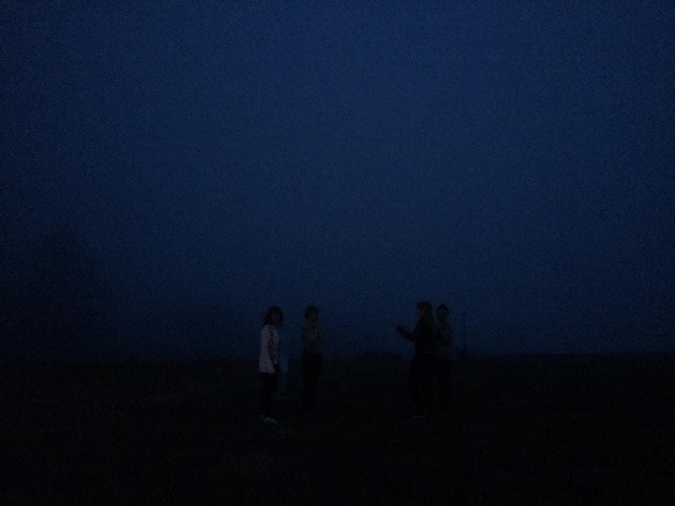 [A deep blue haze of fog in the night. Through the haze some shadowed figures can be made out.]