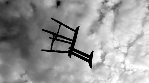 Black-and-white image showing a wooden chair thrown into a cloudy sky.