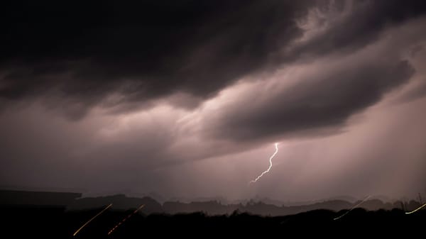 A wide stretch of dark, stormy sky with a bolt of lightning cracking through the ominous clouds.